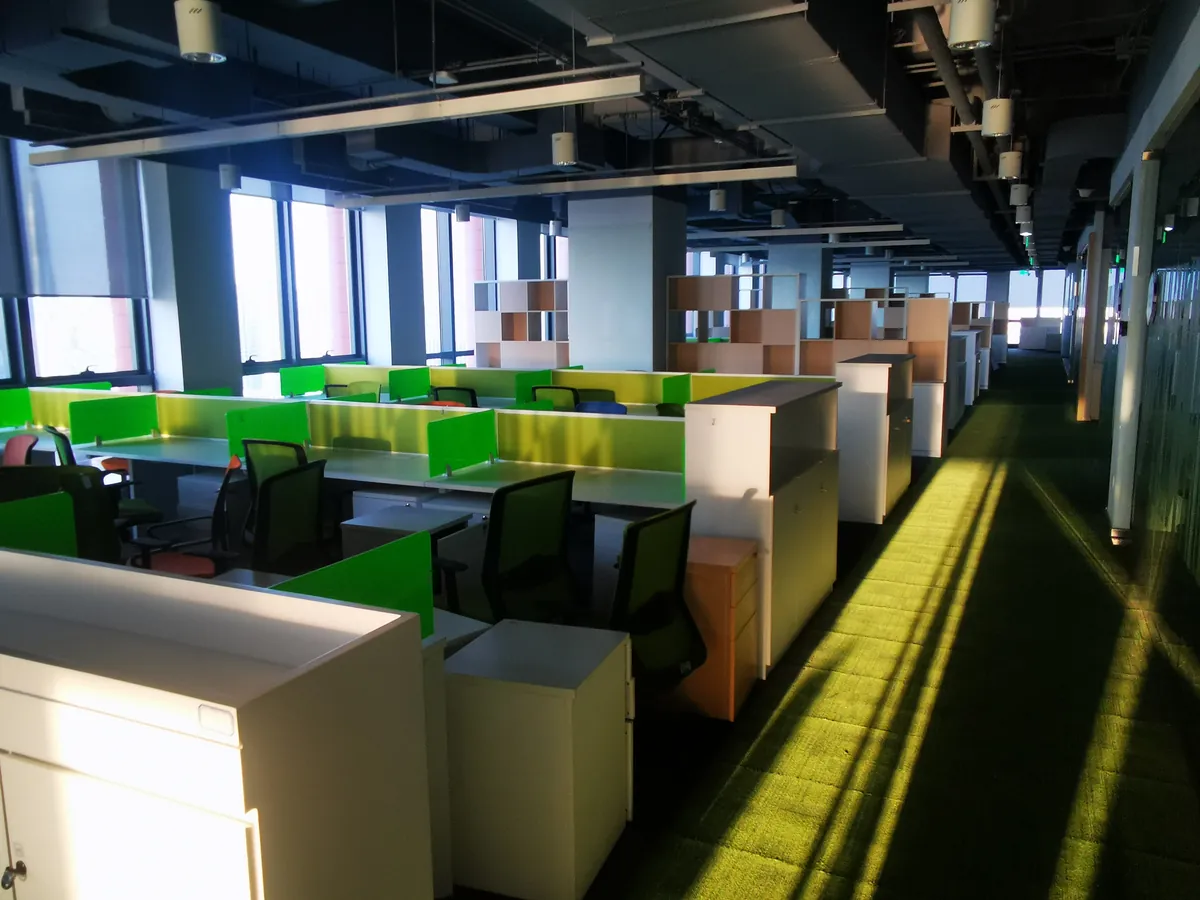 Open-plan hot-desk area with green privacy screens overlooking the Tianjin Binhai skyline — flexible workspace for visiting overseas brand teams and cross-border project staff.