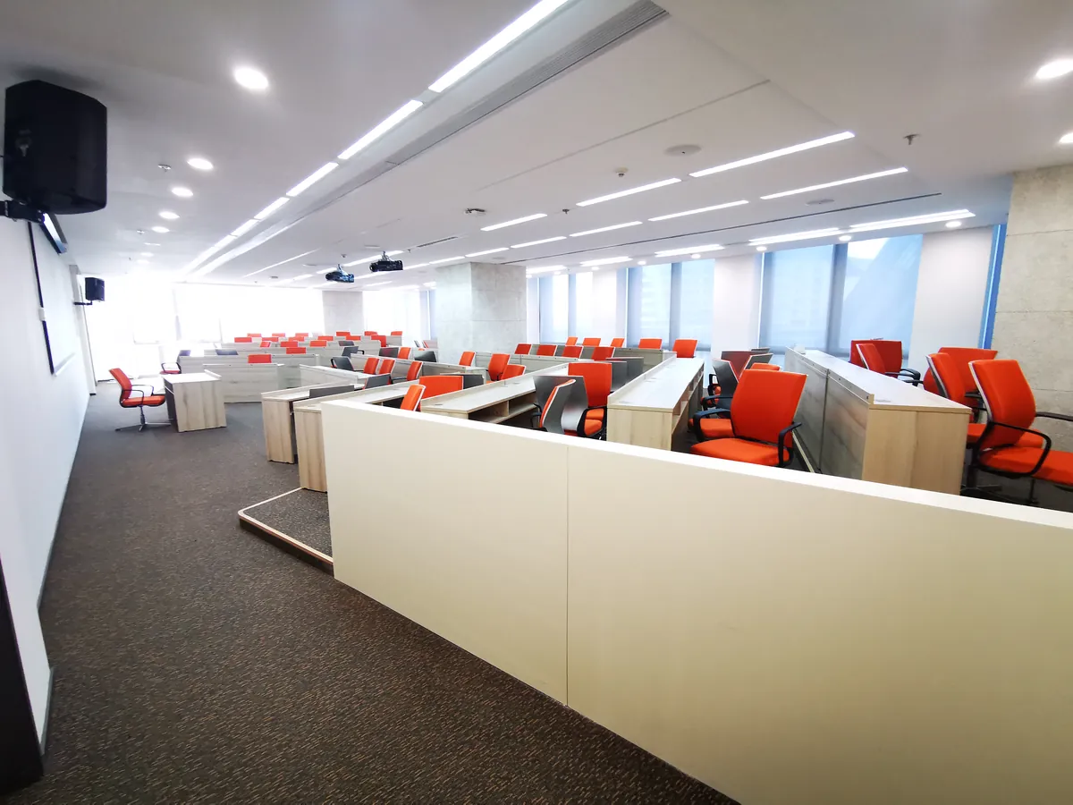 Cross-border e-commerce training room: orange ergonomic chairs at tiered desks, projector and screen for in-house Douyin / Kuaishou operator training.